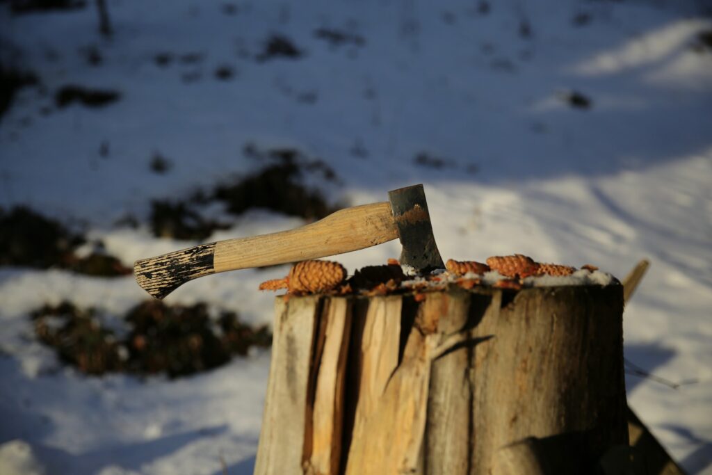 Off grid living wooden axe stabbed on a tree stump on the snow