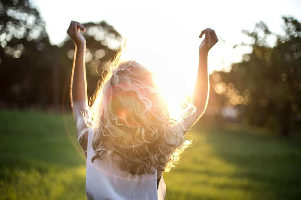 American woman showed from the back raising hands to the sun standing on acres of land