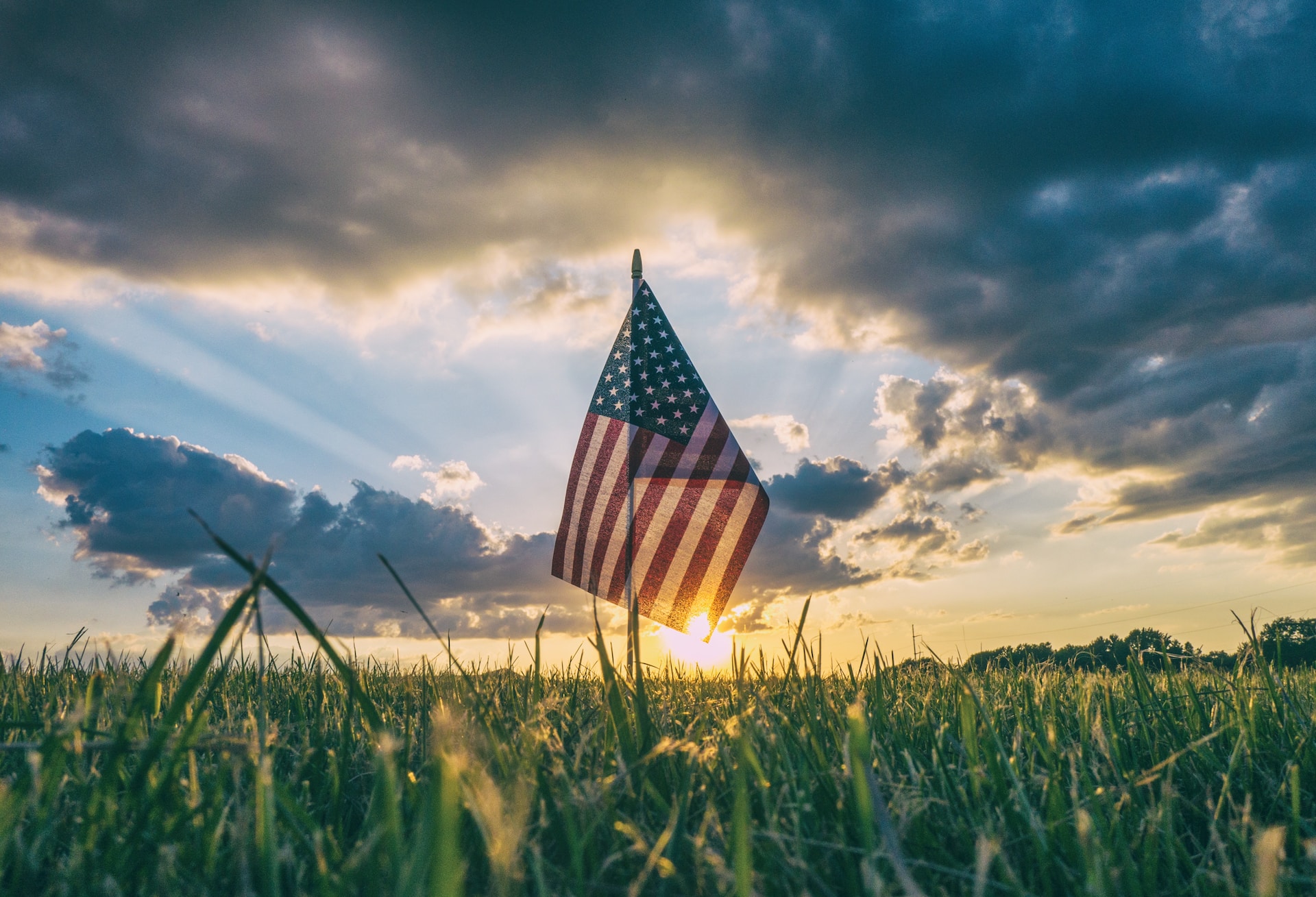 American flag in the grass on cloudy sky at sunset