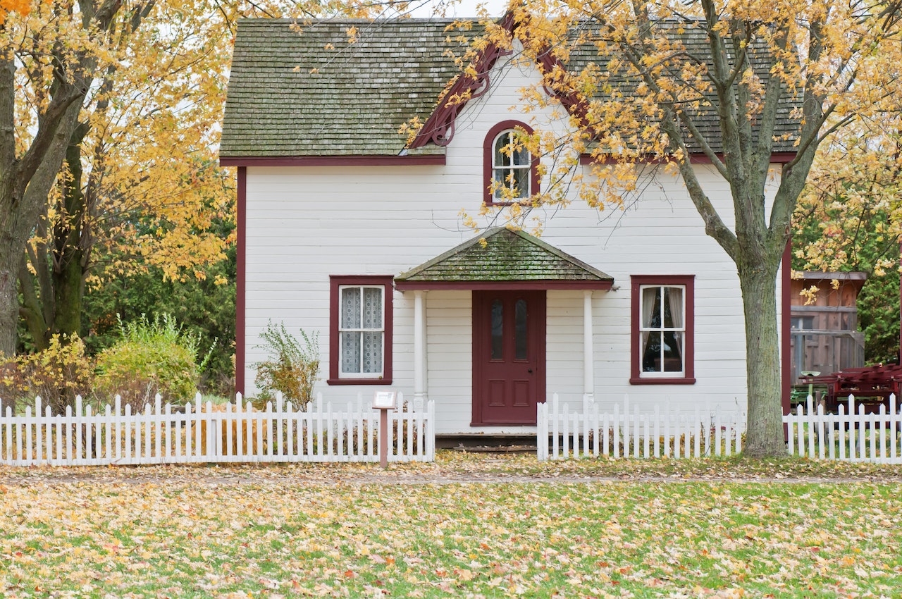 White and Red Wooden House With Fence Surrounded by Trees In Fall